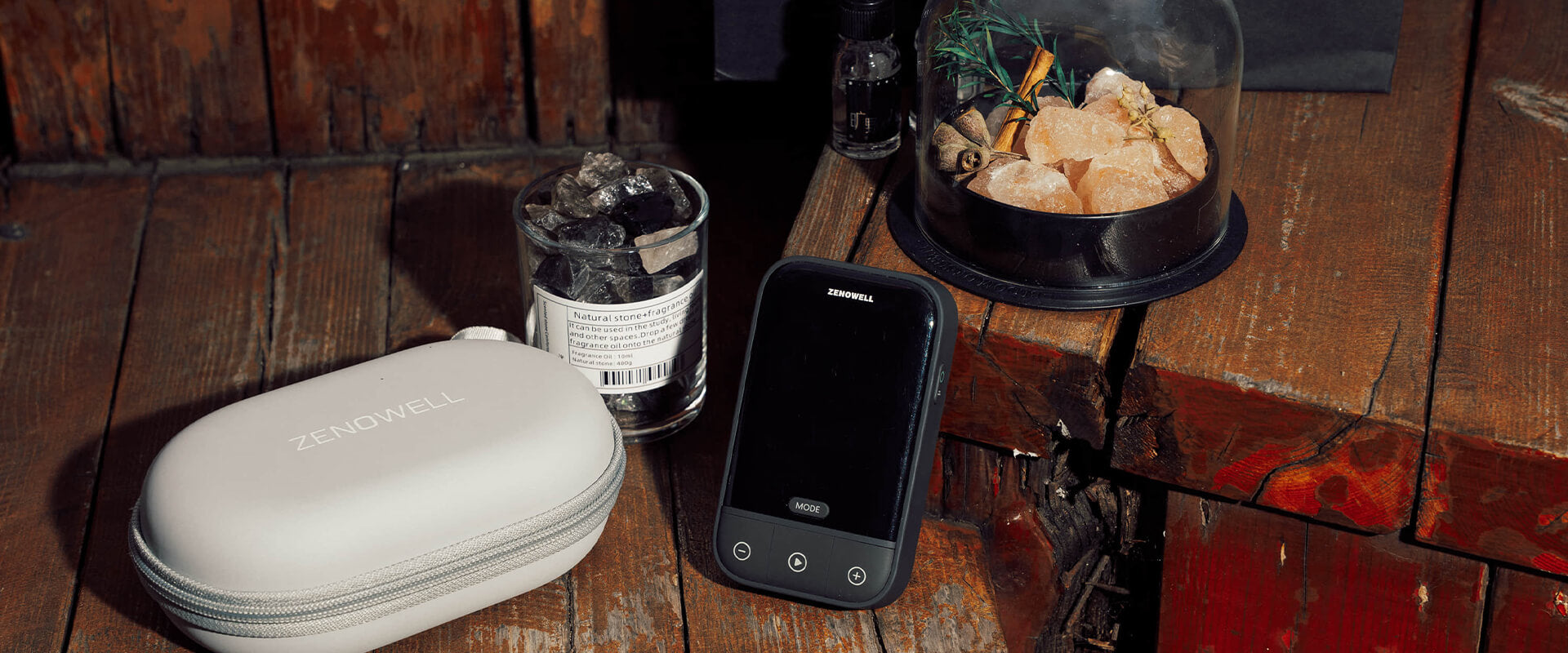 A ZenoWell Vagus nerve stimulation device Vita and box placed beside a fragrance jar and natural stones, resting on a wooden table.